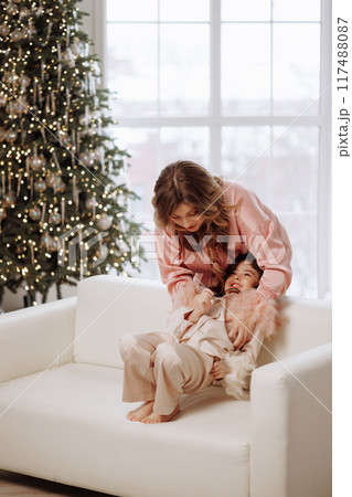 A woman is holding a child on a couch in front of a Christmas tree A woman is holding a child on a couch in front of a Christmas tree 117488087