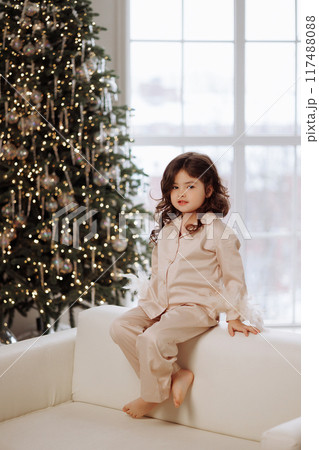 A young girl is sitting on a couch in front of a Christmas tree A young girl is sitting on a couch in front of a Christmas tree 117488088