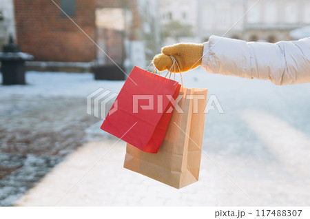 Cropped unrecognizable Woman Holding a red shopping bags, Celebrating Christmas. Female holding a presents ready to celebrate winter holidays at city street. Mock up 117488307