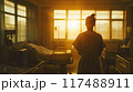 In a sunlit hospital room, a figure gazes out at the golden light 117488911