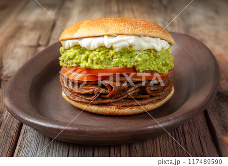 CHILEAN FOOD. Sandwich Churrasco italiano on colors of italian flag. Popular sandwich with round bread, beef, avocado guacamole, tomatoes and mayonnaise CHILEAN FOOD. Sandwich Churrasco italiano on colors of italian flag. Popular sandwich with round bread, beef, avocado guacamole, tomatoes and mayonnaise 117489590