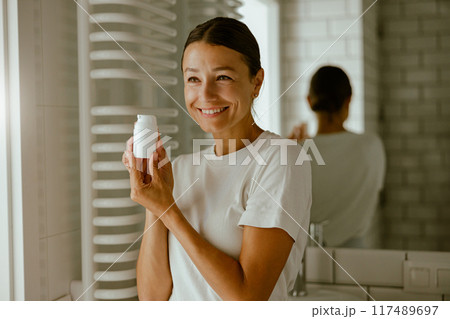A Radiant Woman Graciously Holding a Skincare Product in a Sleek, Modern Bathroom Setting 117489697