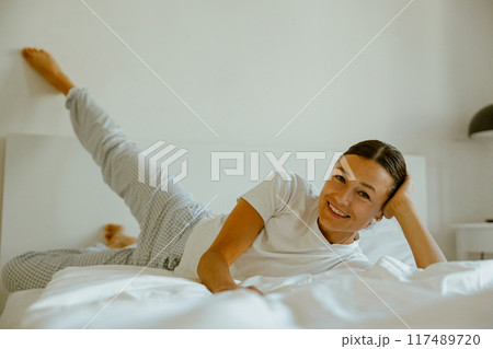 A Relaxing Woman in Bed with a Delightfully Playful Pose for Comfort and Serenity A Relaxing Woman in Bed with a Delightfully Playful Pose for Comfort and Serenity 117489720