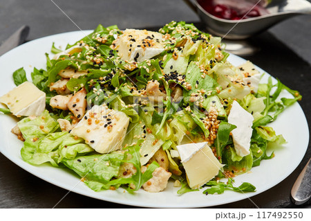 Fresh green salad with chicken, brie cheese, and sesame seeds, served with berry sauce on the side 117492550