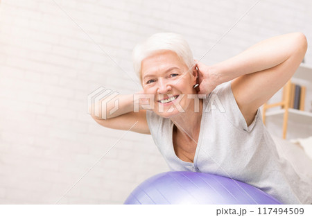 Happy active mature woman doing exercises with fitness ball at home, free space Happy active mature woman doing exercises with fitness ball at home, free space 117494509