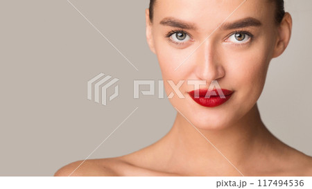 A woman with striking red lips is confidently posing for a camera, exuding charm and elegance. Her poised demeanor and bold makeup enhance the allure of the image, copy space 117494536