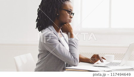 Black lady is working diligently on her laptop at her office desk. The environment is calm and organized, with a modern feel, highlighting her dedication. Black lady is working diligently on her laptop at her office desk. The environment is calm and organized, with a modern feel, highlighting her dedication. 117494649