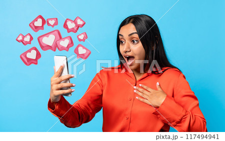 Amazed Indian millennial woman texting lover on smartphone, expressing wow emotion on blue background. Modern digital communication, dating mobile app concept Amazed Indian millennial woman texting lover on smartphone, expressing wow emotion on blue background. Modern digital communication, dating mobile app concept 117494941