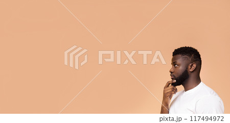 African American man with a short beard and short haircut is shown in profile, thinking, against a peach background. He is looking at copy space, panorama African American man with a short beard and short haircut is shown in profile, thinking, against a peach background. He is looking at copy space, panorama 117494972