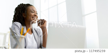 Joyous African American businesswoman at her desk, using a laptop in a stylish office environment, panorama with copy space 117495239