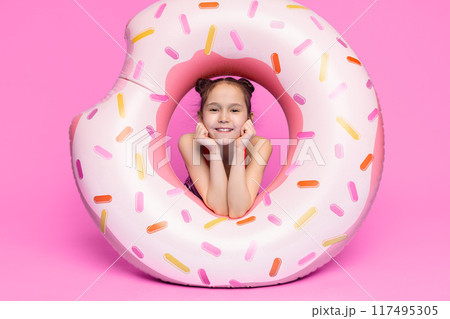 A young female child is seated in a pool float shaped like a donut. The girl is positioned comfortably in the center of the floating device, enjoying the sunny weather and water surroundings. A young female child is seated in a pool float shaped like a donut. The girl is positioned comfortably in the center of the floating device, enjoying the sunny weather and water surroundings. 117495305