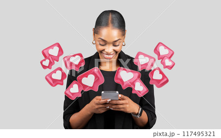 Engaged African American businesswoman in a classic black blazer, smiling while focusing on her smartphone screen against a plain grey background, chatting with lover Engaged African American businesswoman in a classic black blazer, smiling while focusing on her smartphone screen against a plain grey background, chatting with lover 117495321
