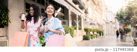 Two Happy Multiethnic Girlfriends Walking With Shopping Bags On City Street, Young Cheerful Women Carrying Purchases And Drinking Takeaway Coffee, Enjoying Seasonal Sales, Copy Space Two Happy Multiethnic Girlfriends Walking With Shopping Bags On City Street, Young Cheerful Women Carrying Purchases And Drinking Takeaway Coffee, Enjoying Seasonal Sales, Copy Space 117495368