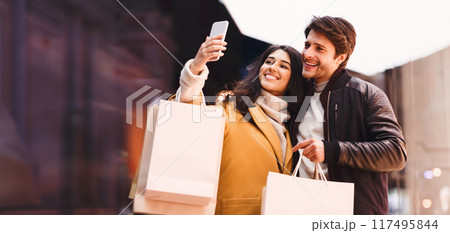 Young couple taking selfie after shopping in city mall, walking outdoors in the evening Young couple taking selfie after shopping in city mall, walking outdoors in the evening 117495844