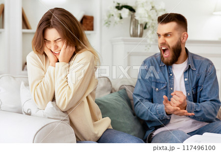 Couple Arguing. Husband Shouting To Desperate Wife, Sitting On Couch At Home 117496100