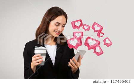 Multitasking millennial caucasian businesswoman in a stylish black suit browsing her smartphone with a smile while enjoying a hot beverage, texting her lover 117496462