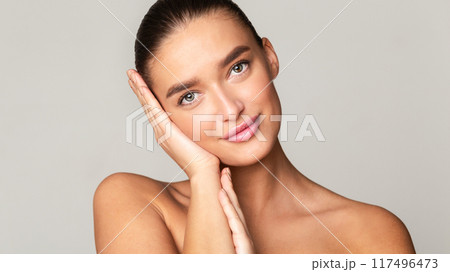 A beautiful young woman with long hair posing for a portrait. She is holding her hands against her cheeks, emphasizing her features. With a calm expression, she gazes directly at the camera. A beautiful young woman with long hair posing for a portrait. She is holding her hands against her cheeks, emphasizing her features. With a calm expression, she gazes directly at the camera. 117496473