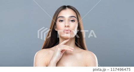 A woman with long brown hair is striking a pose for the camera. She stands confidently, gazing directly at the lens with a slight smile. Her hair cascades down her shoulders 117496475