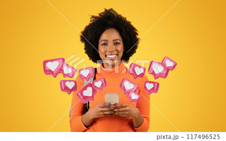 Smiling millennial African American woman with curly hair, wearing an orange turtleneck, texts boyfriend on her phone while carrying a grey backpack on a vibrant yellow background, studio Smiling millennial African American woman with curly hair, wearing an orange turtleneck, texts boyfriend on her phone while carrying a grey backpack on a vibrant yellow background, studio 117496525