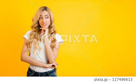 This image features a young woman with long blonde hair, wearing a white t-shirt and blue jeans, standing against a bright yellow background. She is looking to copy space 117496613