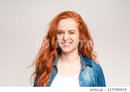 A cheerful young woman with flowing red hair is captured mid-laugh, exhibiting a toothy smile and squinted eyes that express genuine joy A cheerful young woman with flowing red hair is captured mid-laugh, exhibiting a toothy smile and squinted eyes that express genuine joy 117496639