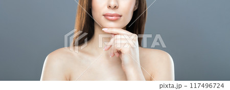 Cropped of woman with long brown hair and bare shoulders thoughtfully touches her chin. The background is gray, and she is lit with studio lighting, web-banner 117496724