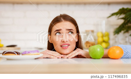 Dieting Concept. Young Woman Choosing Between Fruits and Sweets 117496835