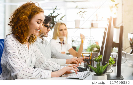 Several coworkers are seated at a desk, each engrossed in their computer screens, actively typing and clicking. The group appears focused and concentrated on their tasks Several coworkers are seated at a desk, each engrossed in their computer screens, actively typing and clicking. The group appears focused and concentrated on their tasks 117496886