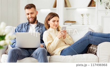A man and woman are seated on a couch, attentively looking at a laptop screen. 117496968