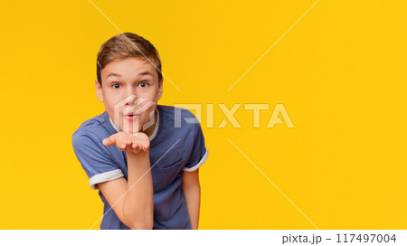 Affection feelings. Cute lovely caucasian boy sending blow kiss with pout lips at camera, orange studio background 117497004