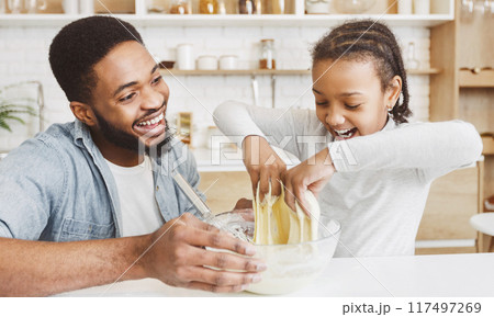 Excited african father and his joyful daughter playing with dough while making pastry at kitchen Excited african father and his joyful daughter playing with dough while making pastry at kitchen 117497269