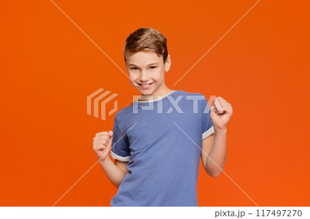 Sly boy making silly grimace, thinking about joke, orange panorama background with empty space 117497270