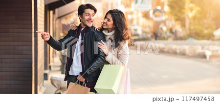 A man and woman are standing on a city street holding shopping bags. 117497458