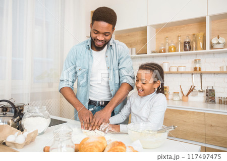 Happy african american father and daughter kneading dough for pastry at home kitchen, copy space 117497475