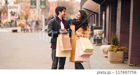 Loving couple waiting for taxi after shopping in city center, walking with bags outdoors, free space 117497756
