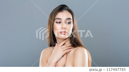 A young woman with straight, long brown hair poses with her hand on her chest against a gray backdrop in a well-lit studio during the daytime. She appears thoughtful and composed A young woman with straight, long brown hair poses with her hand on her chest against a gray backdrop in a well-lit studio during the daytime. She appears thoughtful and composed 117497785