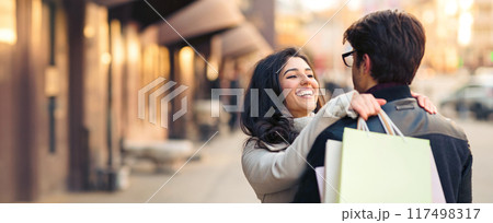 A man and woman are walking on a busy city street, both holding shopping bags in their hands. A man and woman are walking on a busy city street, both holding shopping bags in their hands. 117498317