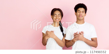 Kind-hearted teens holding their hands togehter on chest being thankful, pink background 117498332