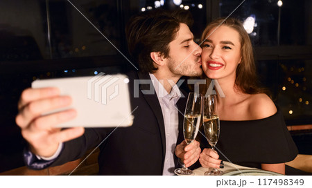 Portrait of kissing couple making selfie photo with smart phone during romantic dinner in restaurant Portrait of kissing couple making selfie photo with smart phone during romantic dinner in restaurant 117498349