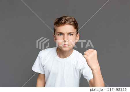 This image captures a teenager clenching his fist in determination or defiance, with a focused look, isolated against a grey backdrop 117498385