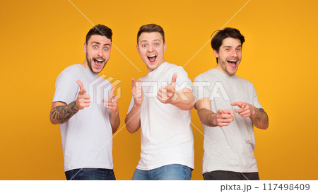 Gotcha. Excited friends pointing fingers at camera over orange background 117498409
