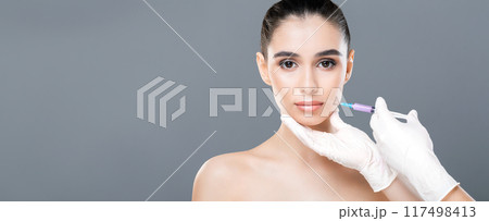A woman with a serious expression is receiving a cosmetic injection in a clinic. A medical professional with gloves carefully administers the treatment, copy space A woman with a serious expression is receiving a cosmetic injection in a clinic. A medical professional with gloves carefully administers the treatment, copy space 117498413