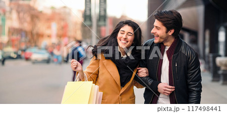 Excited couple doing shopping on weekend together, talking and laughing outdoors 117498441