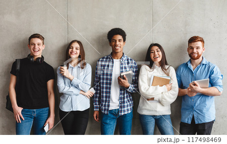 College students with books smiling to camera over grey wall, having break 117498469