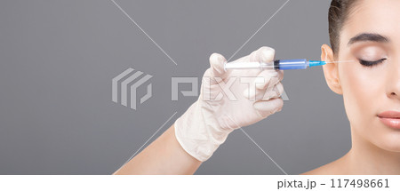 A woman is receiving a filler injection from a specialized doctor in a medical setting. The doctor is carefully administering the injection to the woman face, copy space 117498661