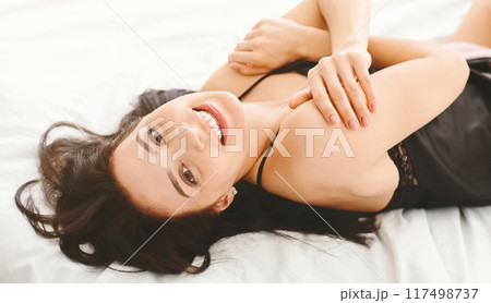 Adorable young millennial woman lying in bed, enjoying her youth and fresh beauty, smiling at camera 117498737