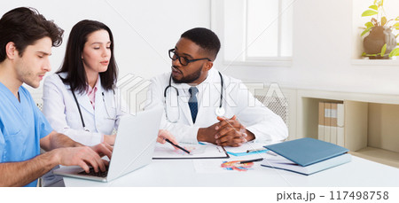 Young medical team discussing reports, using laptop in meeting room 117498758