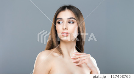A young woman with long, straight hair poses gracefully, looking to her side against a plain gray studio background. Her pose is serene and confident, highlighting her natural beauty and elegance. 117498766