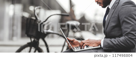Cropped of black man startuper wearing suit using laptop at downtown area, bicycle standing by him, web-banner Cropped of black man startuper wearing suit using laptop at downtown area, bicycle standing by him, web-banner 117498804