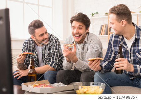 Three mates are sharing pizza and laughter in a bright living room, showcasing european men enjoying their friendship 117498857